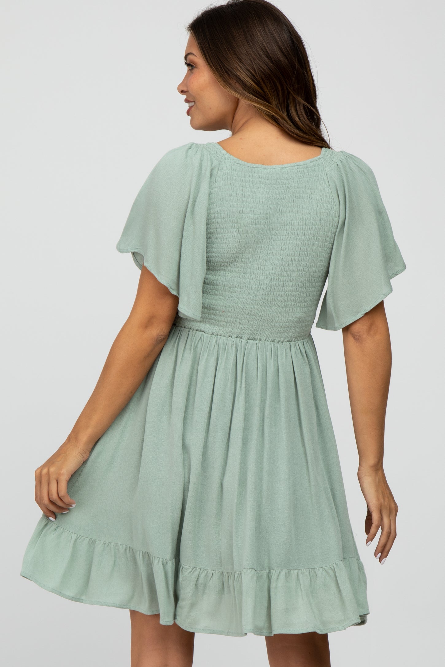 woman wearing a mint green maternity dress with flutter sleeves and a smocked bodice, showing a flowing skirt