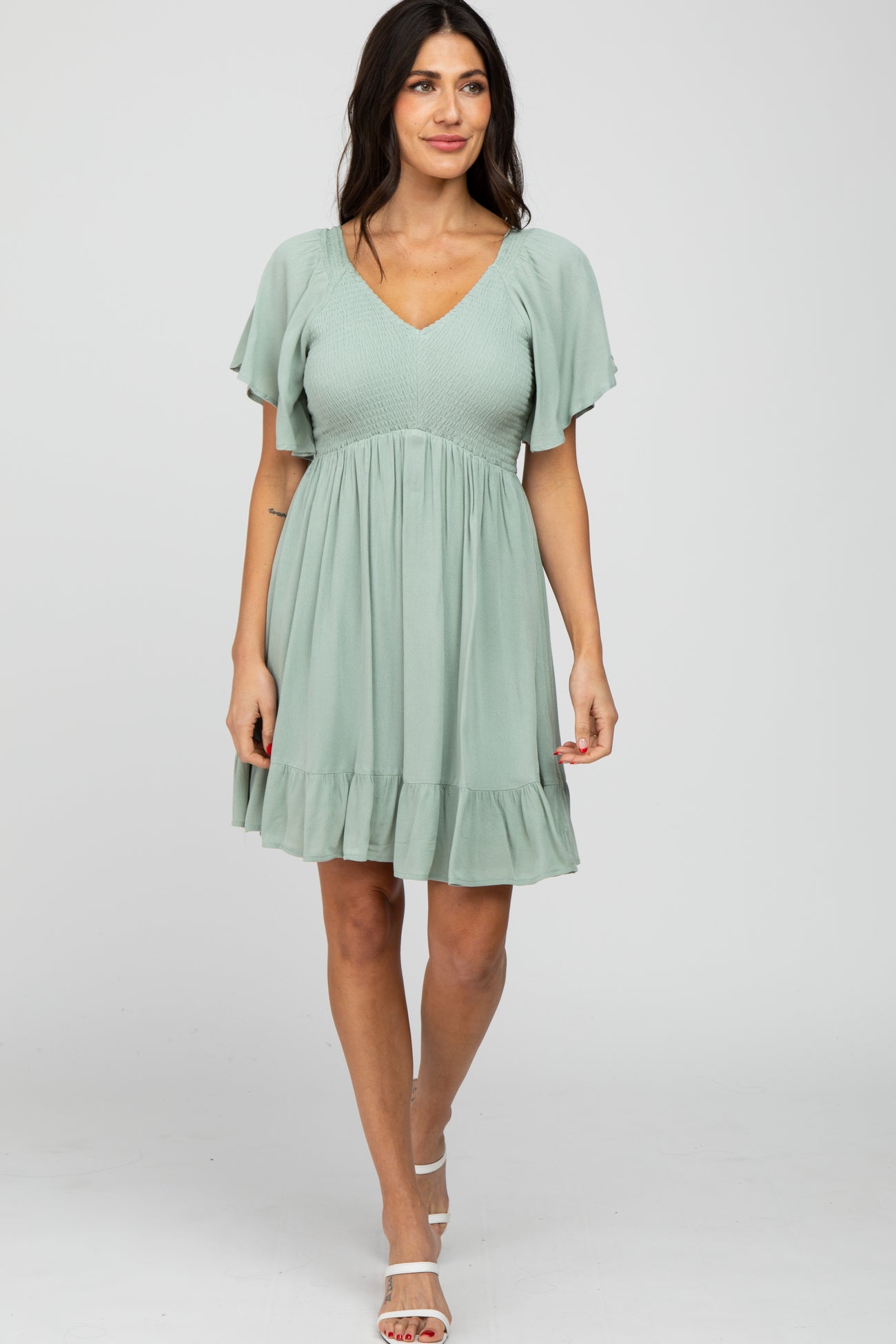 woman wearing a sage green v-neck maternity dress with flutter sleeves and a smocked bodice