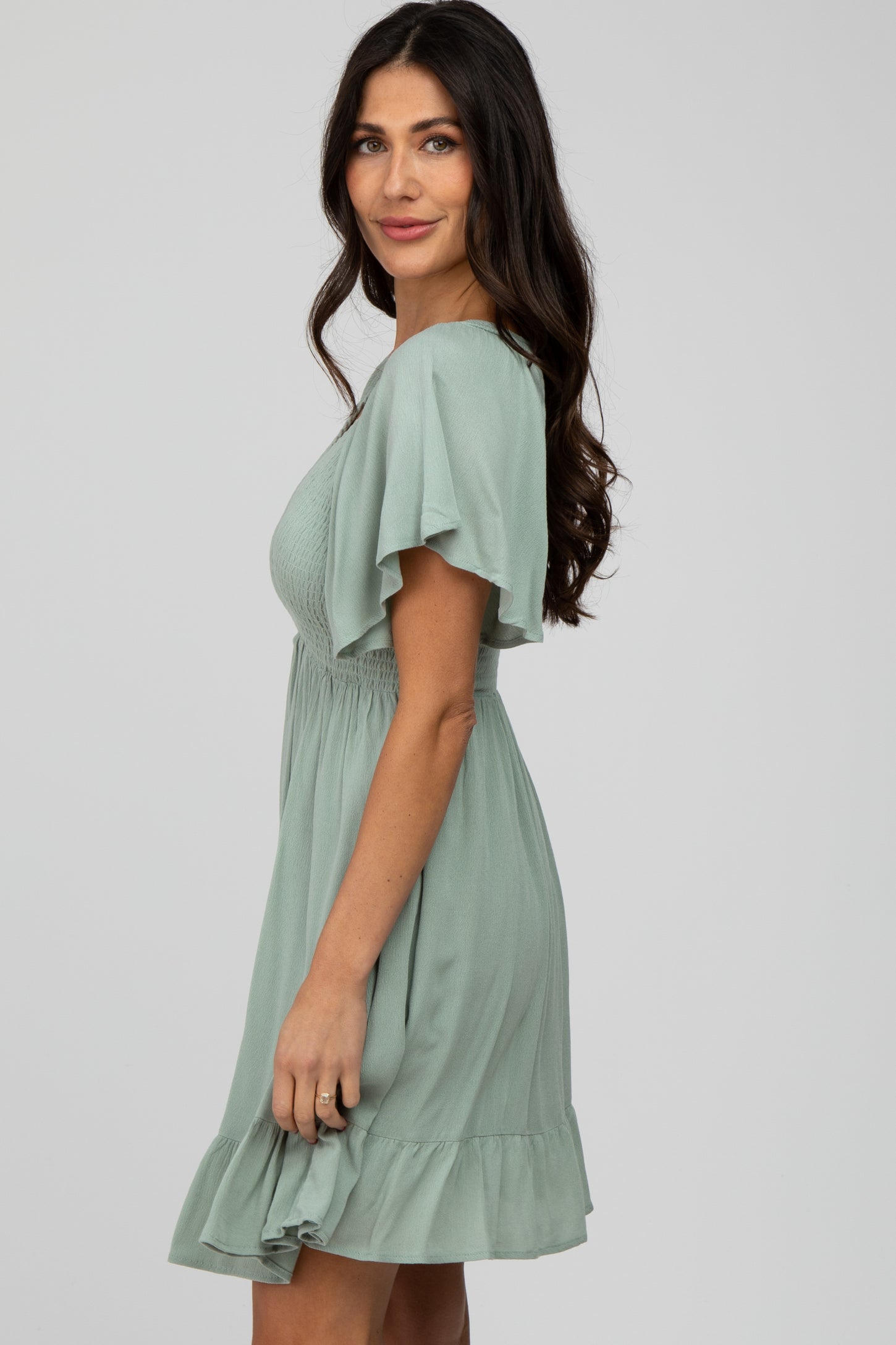 woman wearing a light green short sleeve dress with ruffle hem and smocked waist, posing sideways with a smile