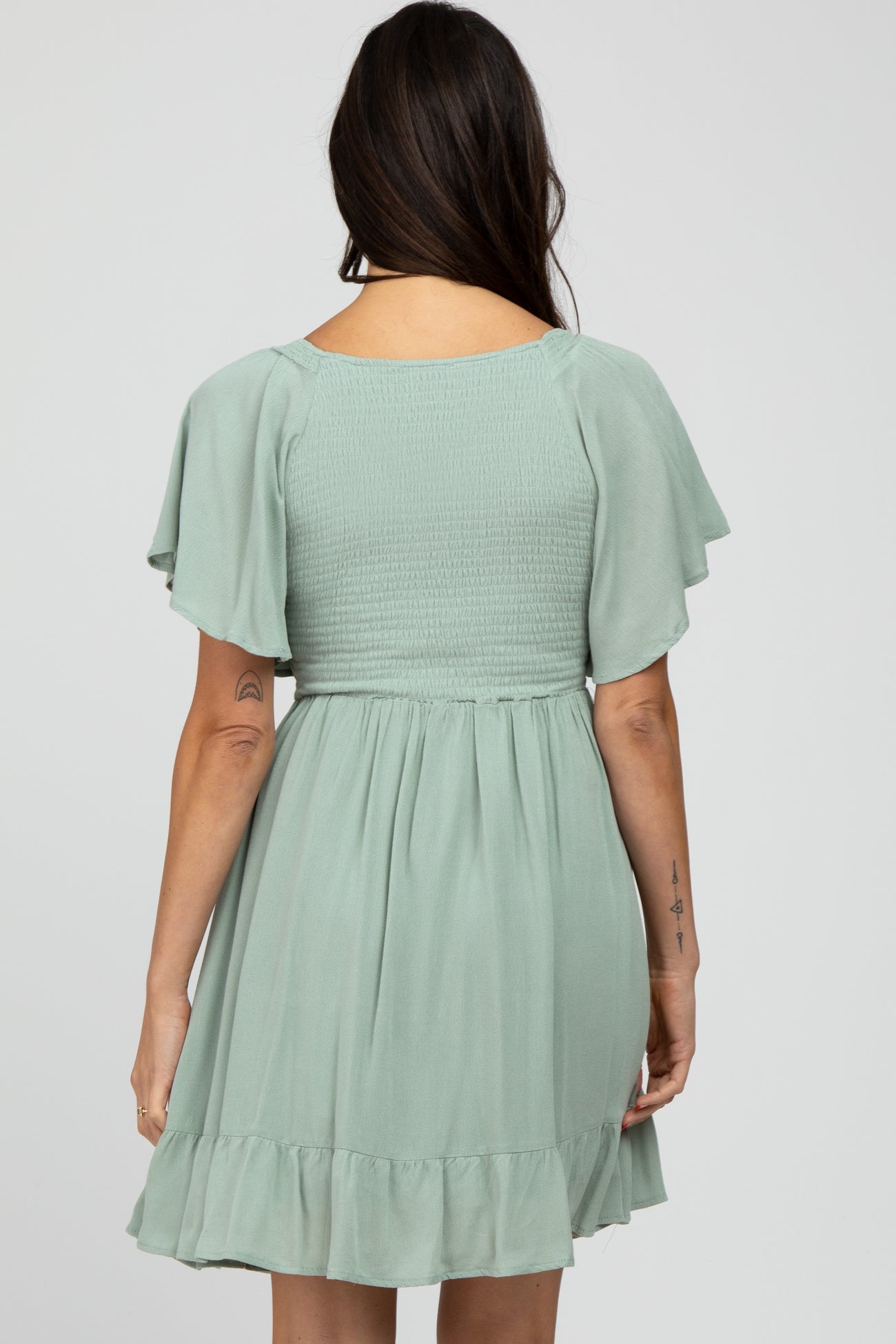 woman wearing a sage green short dress with flutter sleeves and a smocked bodice