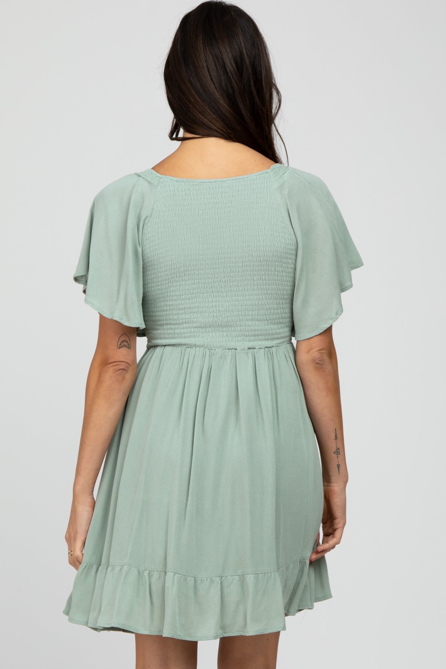 woman wearing a sage green short dress with flutter sleeves and a smocked bodice