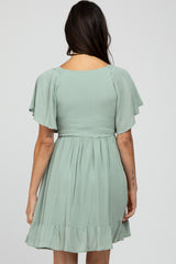 woman wearing a sage green short dress with flutter sleeves and a smocked bodice