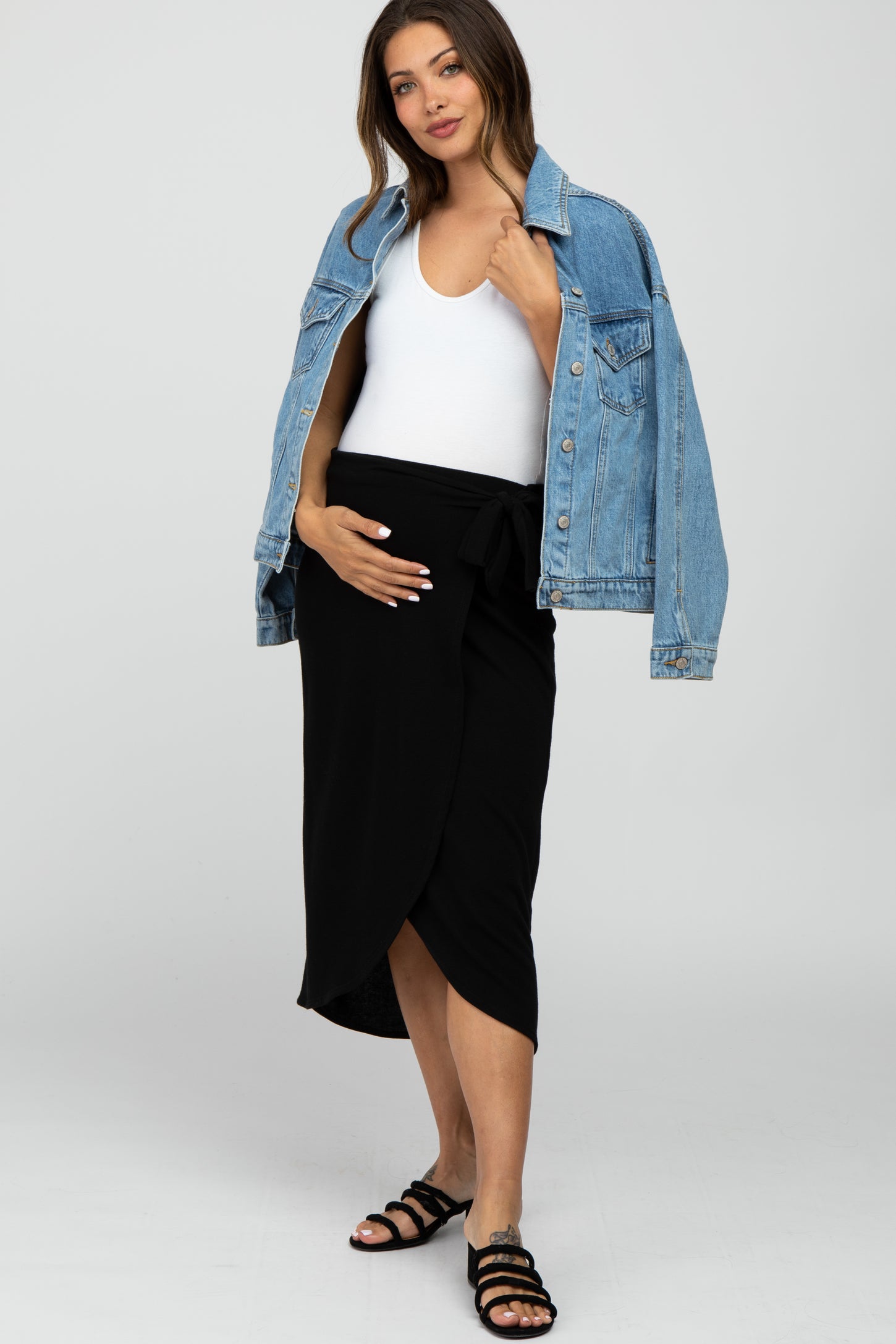 pregnant woman in white top, black maternity wrap skirt, and denim jacket draped over shoulders
