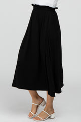 Woman wearing a black flowy midi skirt with a ruffled elastic waistband and white strappy heeled sandals
