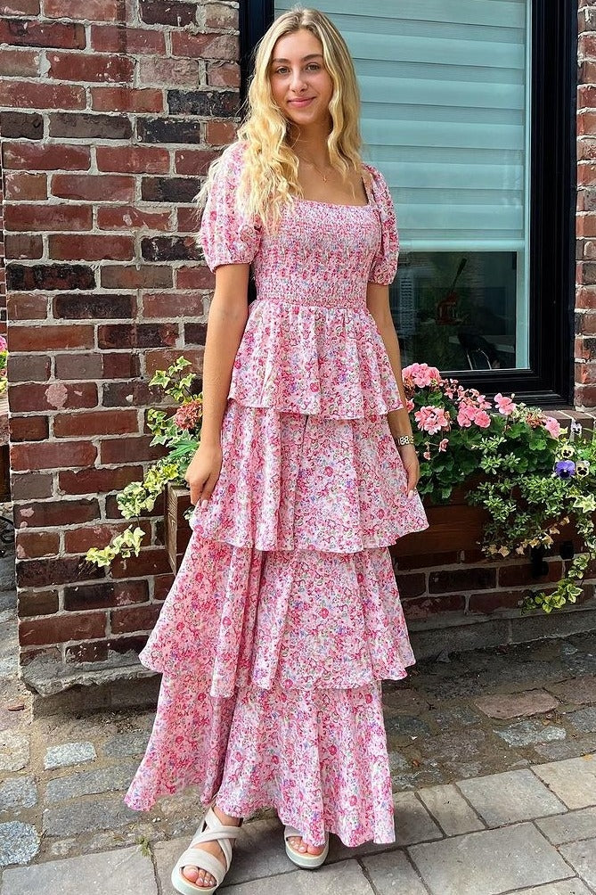 woman wearing a pink floral tiered maxi dress with puff sleeves standing in front of a brick wall