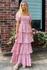woman wearing a pink floral tiered maxi dress with puff sleeves standing in front of a brick wall