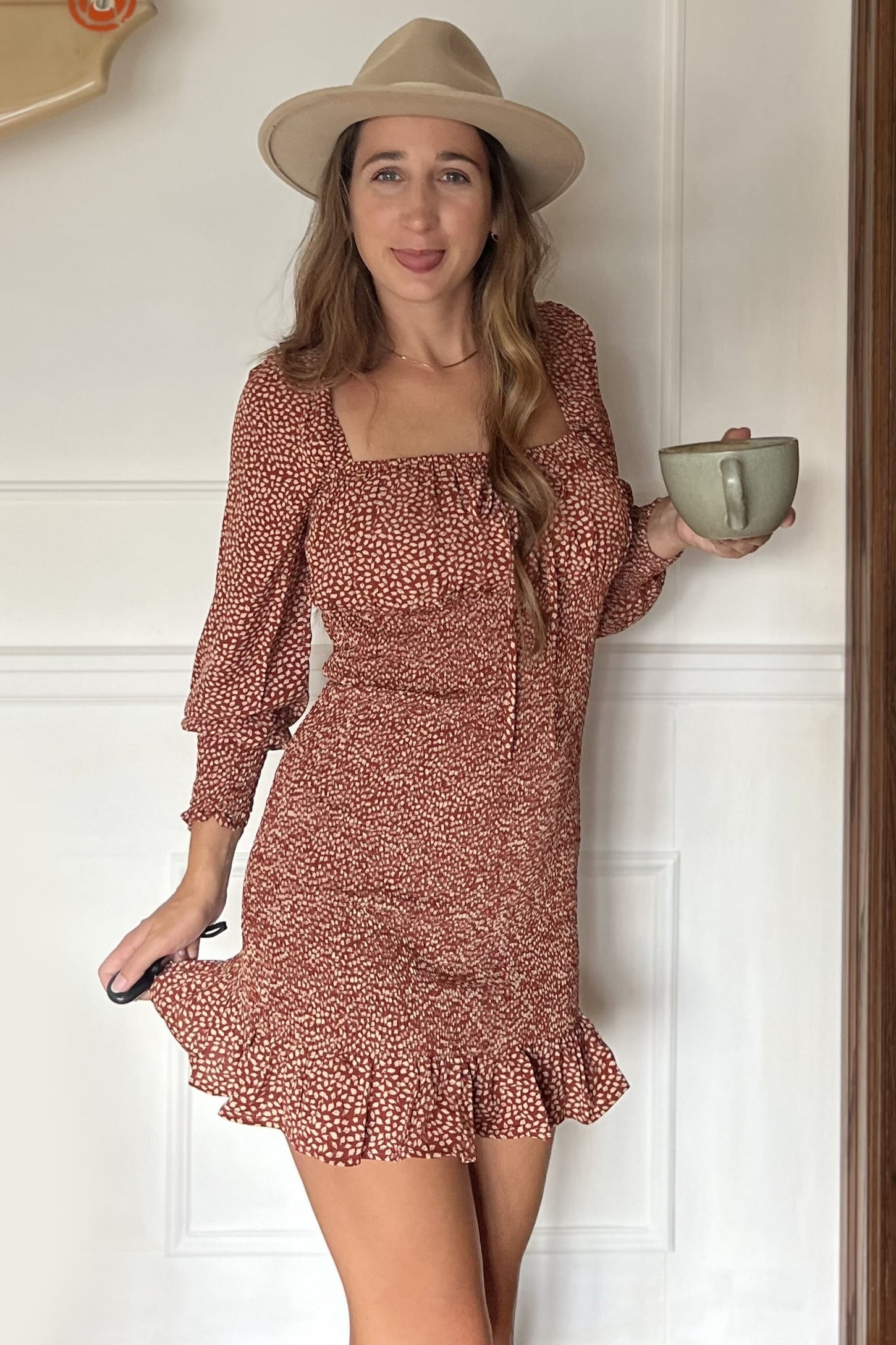 woman wearing a rust floral short dress with ruffle hem and three-quarter sleeves, holding a cup and smiling