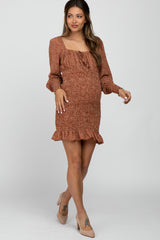 woman wearing a rust floral maternity dress with a ruffled hem and elasticized sleeves, showing her baby bump