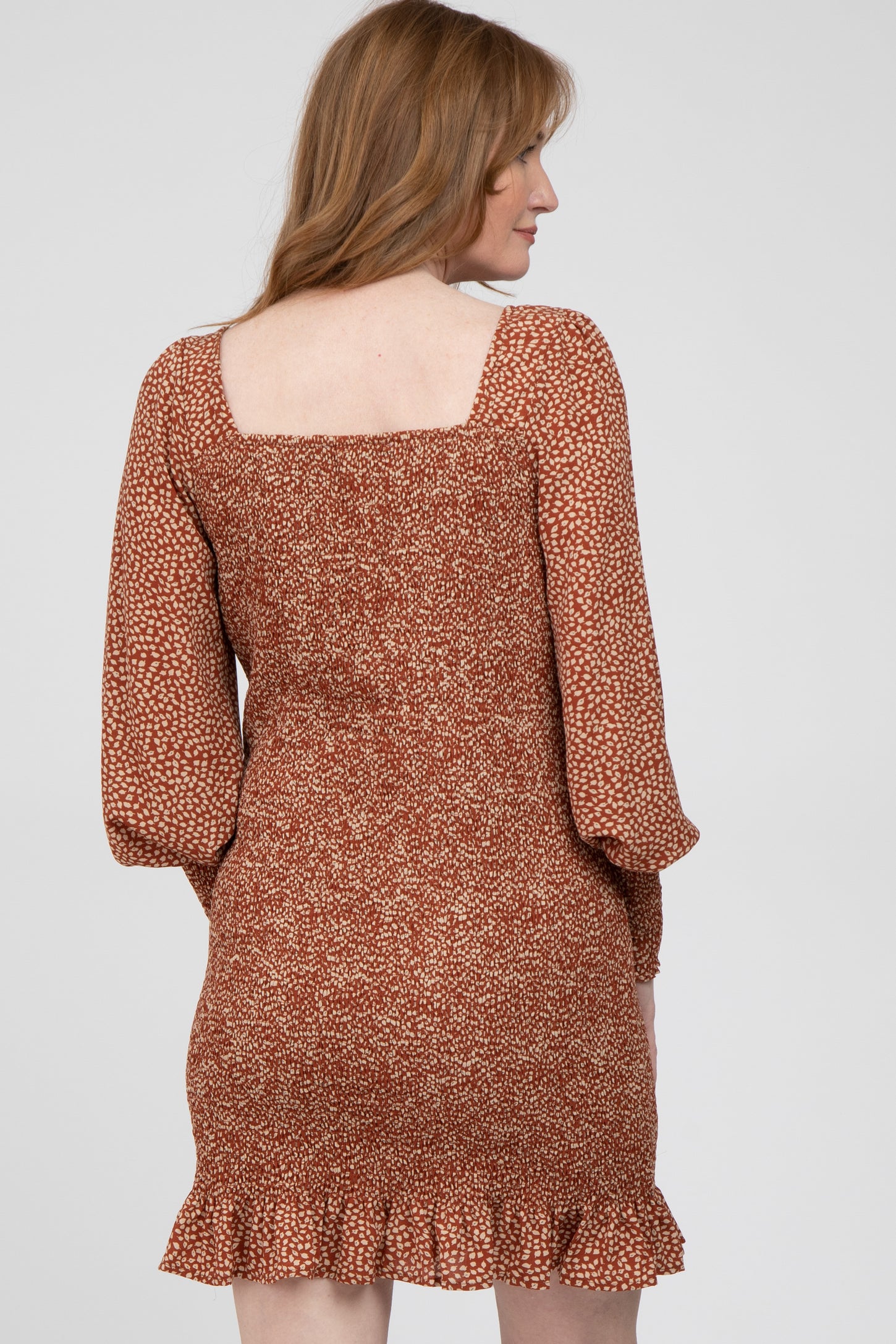 woman wearing a rust-colored floral mini dress with a square neckline and ruffle hem, seen from the back