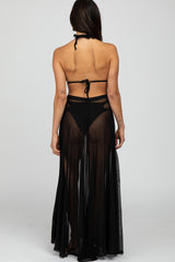 woman wearing a black sheer maxi cover-up with a halter neck, showing an open back and a flowy silhouette