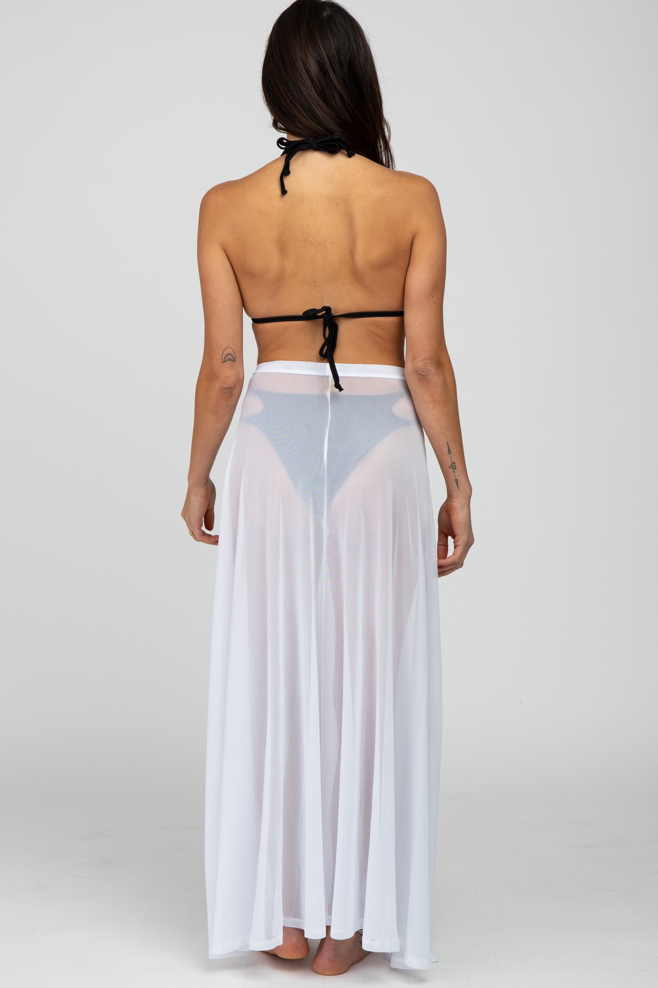 woman wearing a black bikini top and a sheer white long skirt, viewed from the back