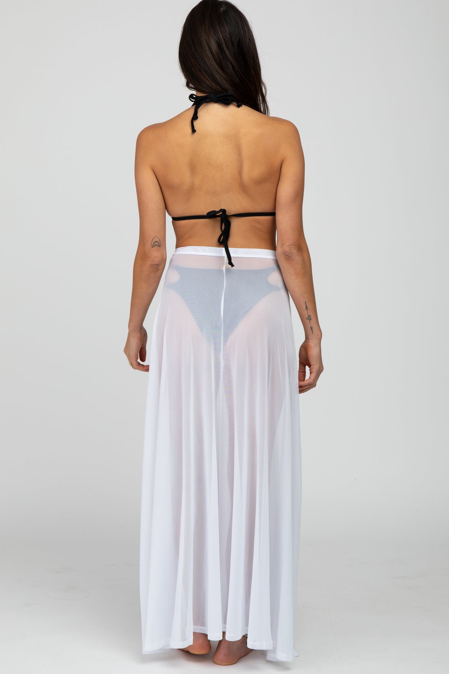 woman wearing a black bikini top and a sheer white long skirt, viewed from the back