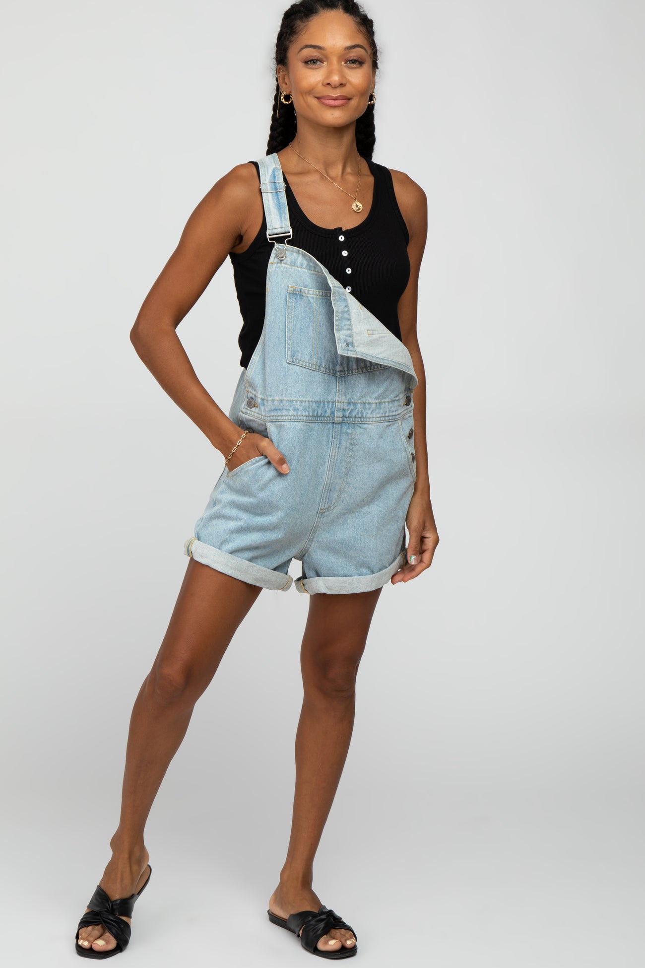 woman wearing a black tank top and light blue denim overalls shorts with rolled hems and black slide sandals