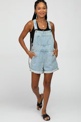 woman wearing a light wash denim overall shorts with rolled cuffs and a black tank top, standing and smiling