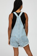 woman wearing a light wash denim overall shorts with rolled hems and a black sleeveless top, seen from the back