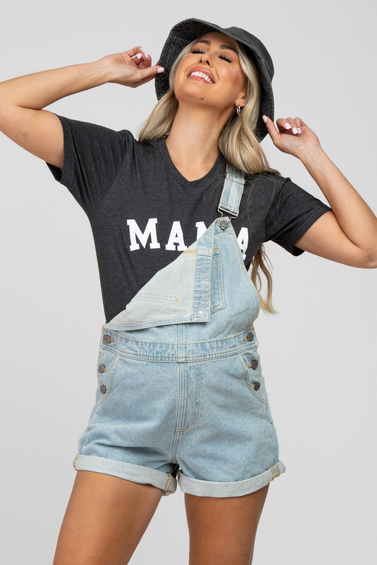 woman wearing a gray maternity t-shirt that says "mama" paired with denim overalls and a black bucket hat