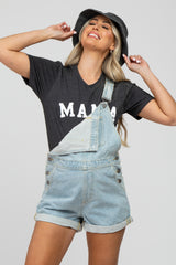 woman wearing a gray maternity t-shirt that says "mama" paired with denim overalls and a black bucket hat