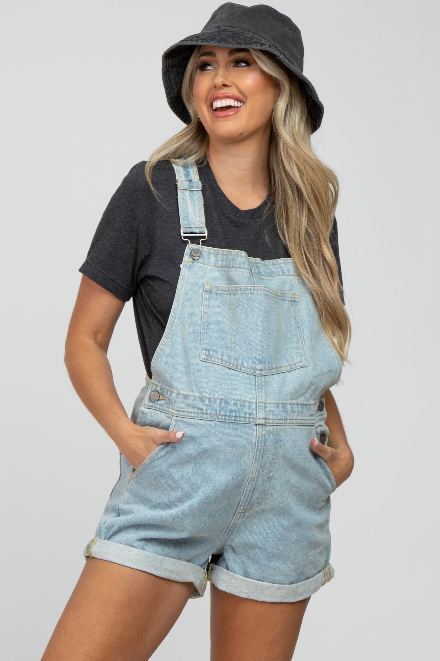 woman wearing a light blue denim maternity overall shorts with rolled cuffs and a black t-shirt, smiling and posing