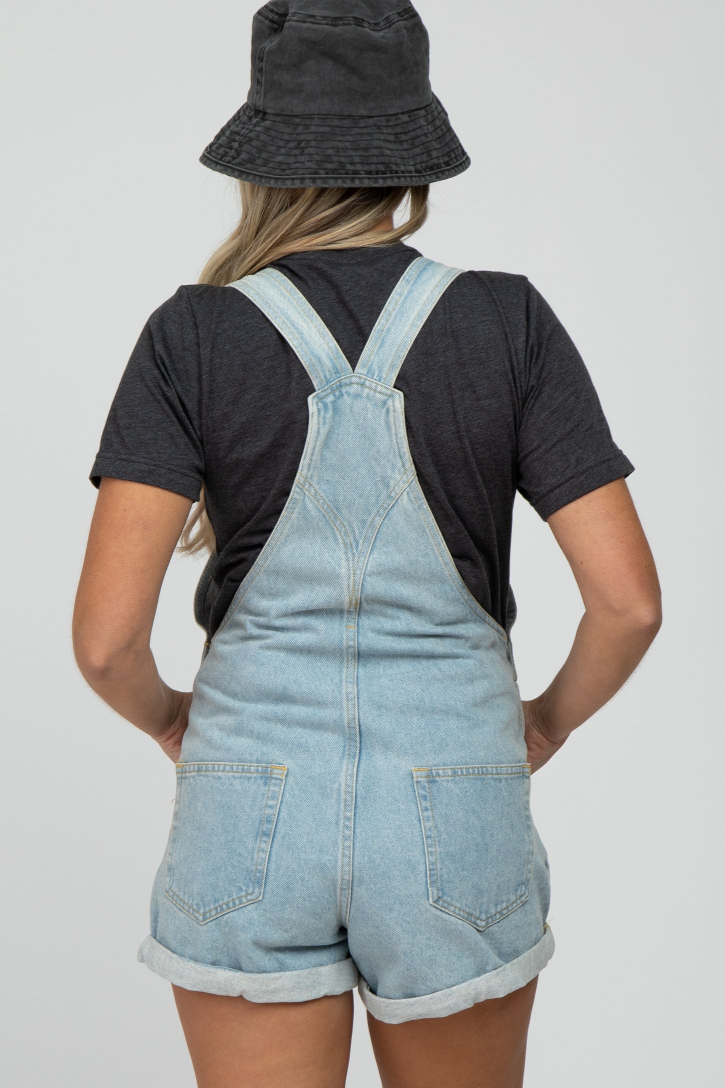 woman wearing a black t-shirt and light wash denim maternity overalls, showing back view
