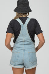 woman wearing a black t-shirt and light wash denim maternity overalls, showing back view