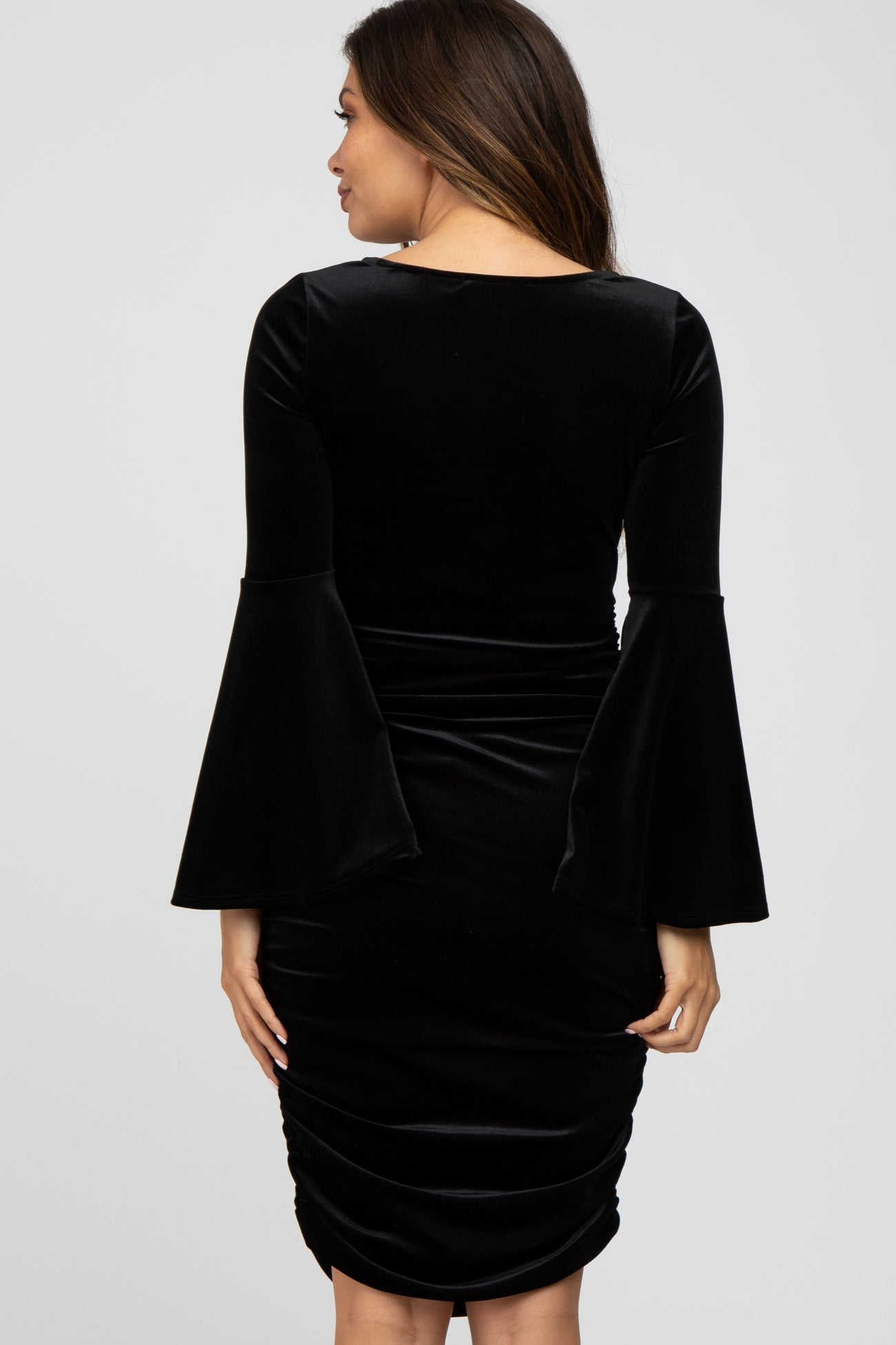 Back view of a woman wearing a black velvet bodycon dress with long bell sleeves and ruched detailing