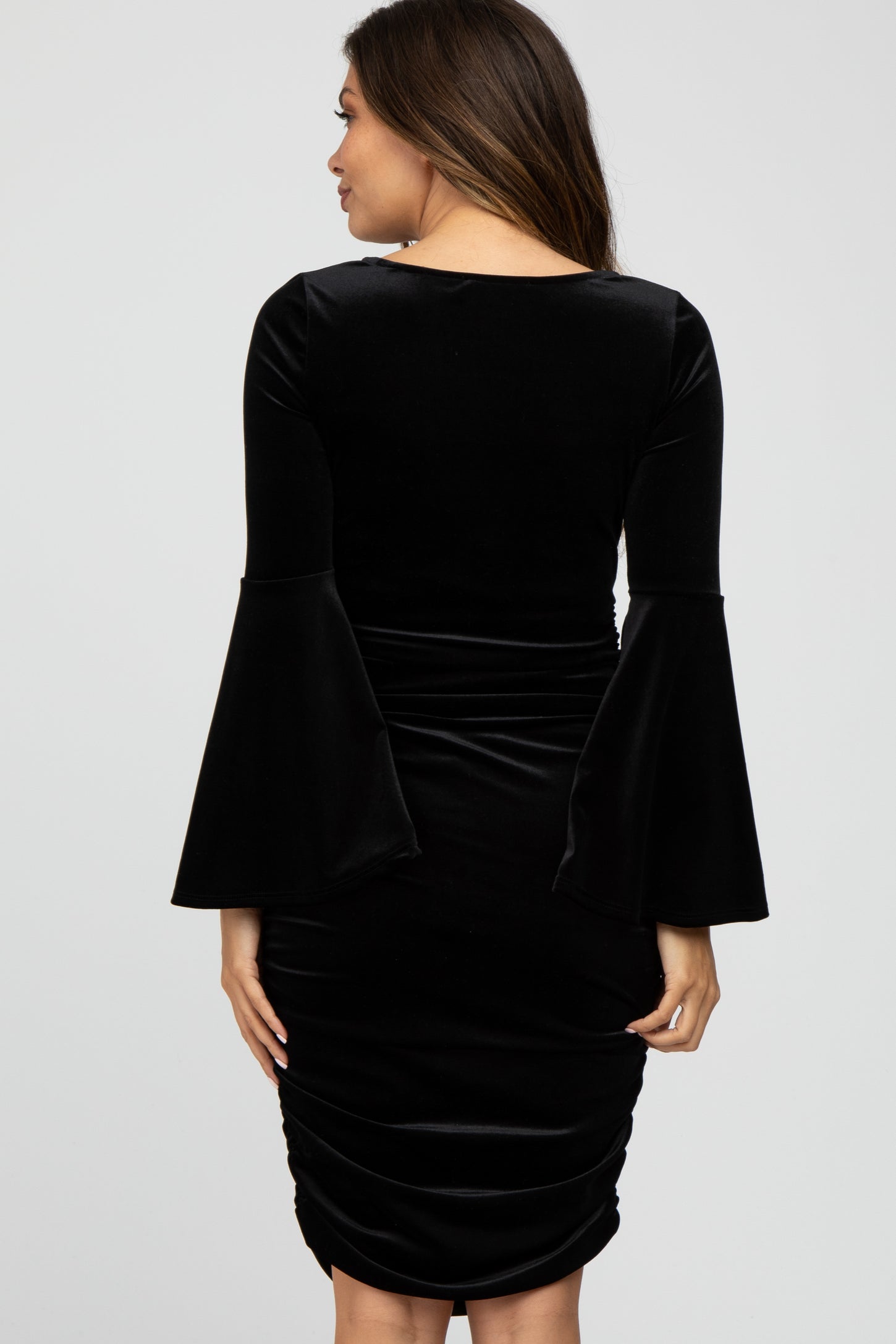 Back view of a woman wearing a black velvet bodycon dress with long bell sleeves and ruched detailing