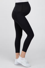 pregnant woman wearing black maternity leggings and white sneakers against a white background