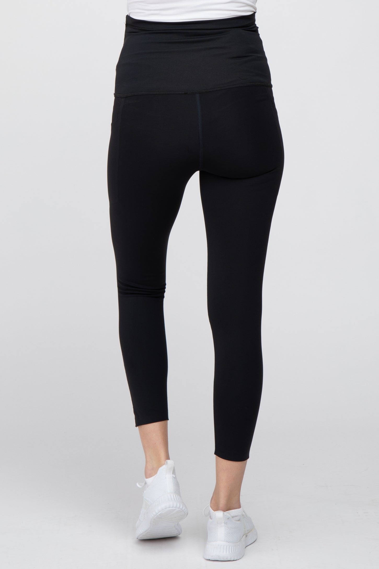 Rear view of person wearing black high-waisted maternity leggings and white sneakers