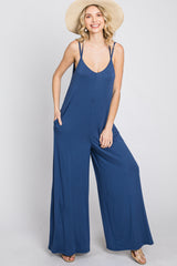 woman wearing a navy blue sleeveless jumpsuit with wide legs and pockets, styled with a straw hat