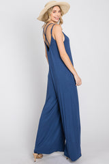 woman wearing a blue sleeveless jumpsuit with stylish back straps and a wide-leg silhouette, holding a straw hat