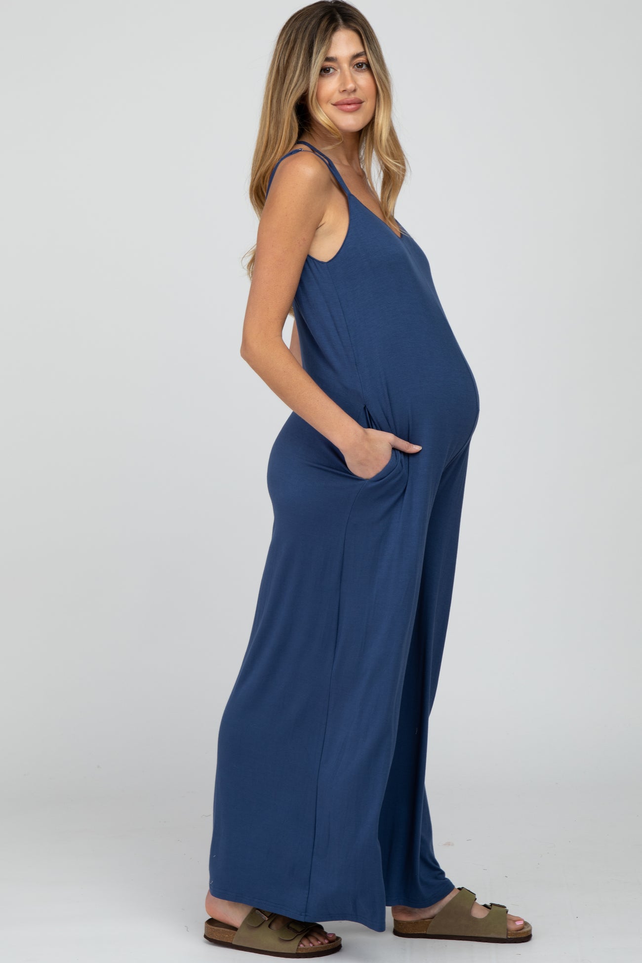 Pregnant woman wearing a blue wide-leg maternity jumpsuit with pockets and spaghetti straps