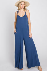 woman wearing a navy blue sleeveless jumpsuit with a wide-leg silhouette and pockets, styled with a straw hat