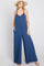 woman wearing a navy blue sleeveless jumpsuit with a wide-leg silhouette and pockets, styled with a straw hat