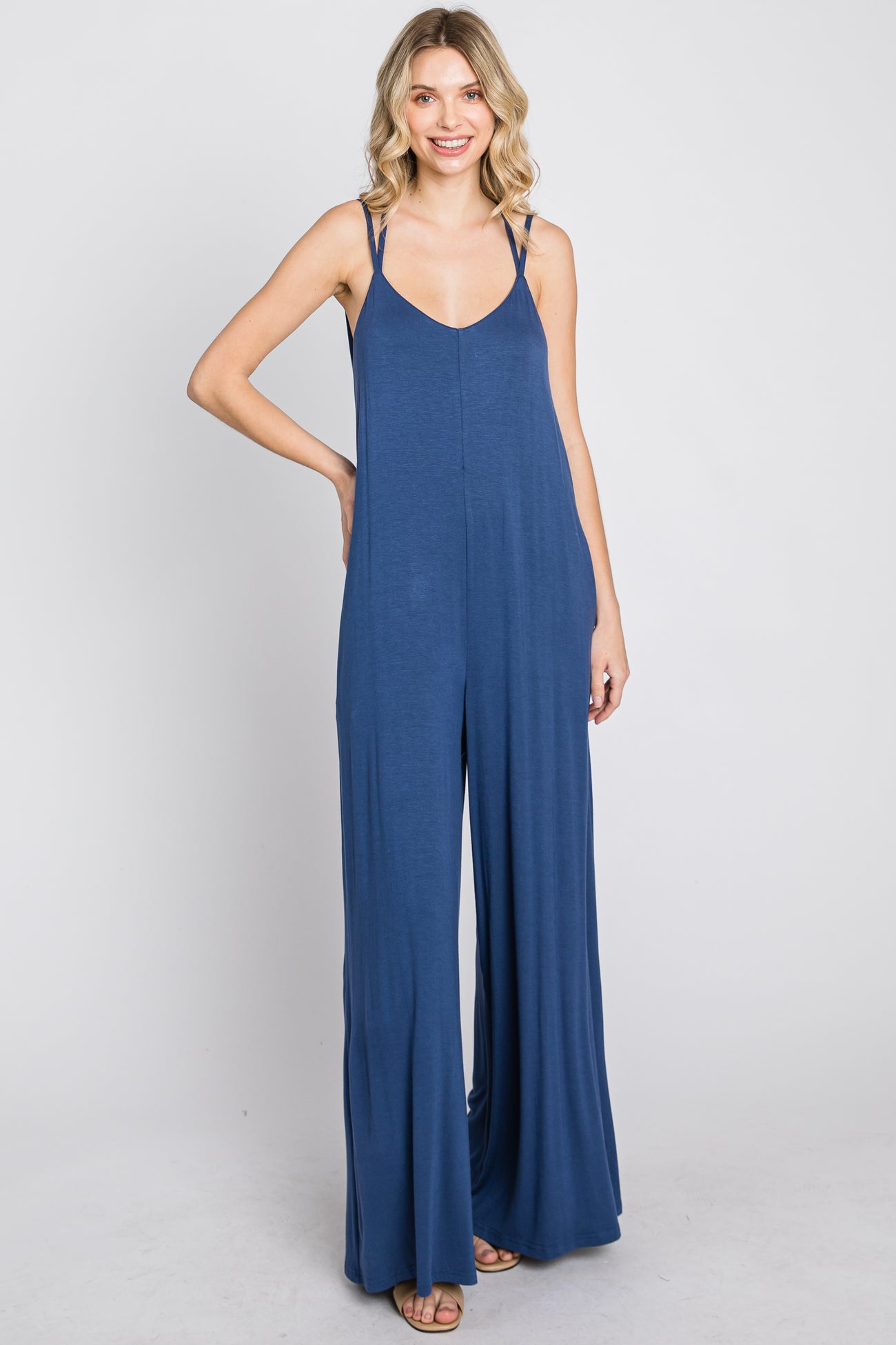 Woman wearing a sleeveless navy blue wide-leg jumpsuit with spaghetti straps against a white background