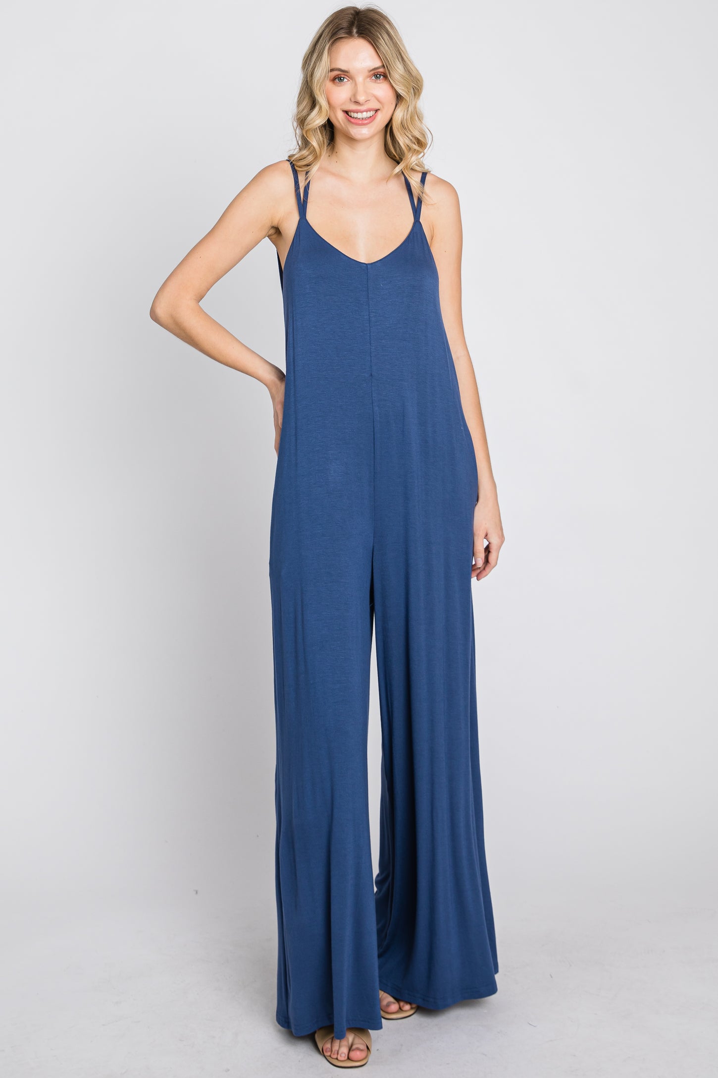 Woman wearing a sleeveless navy blue wide-leg jumpsuit with spaghetti straps against a white background