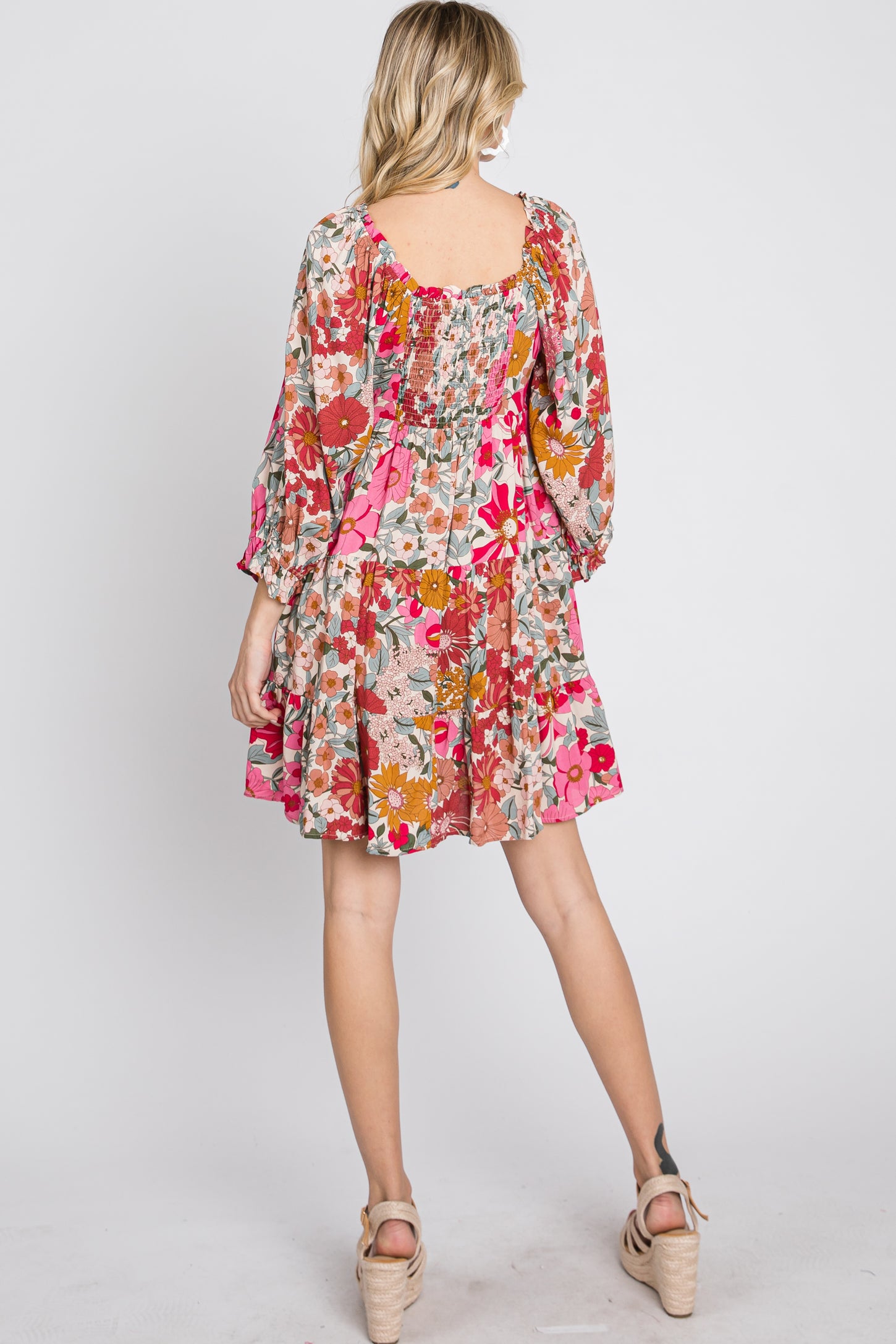 Back view of a woman wearing a colorful floral print mini dress with long sleeves and smocked back detailing