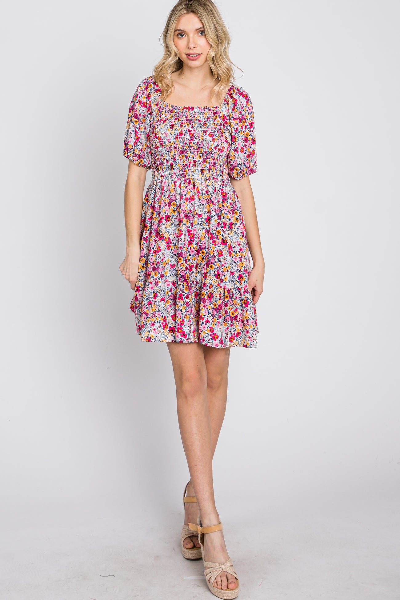 Woman wearing a pink and orange floral mini dress with a smocked bodice and short sleeves