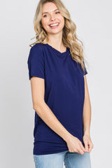 woman wearing a navy blue short sleeve top with a draped neckline and smiling while standing against a light background