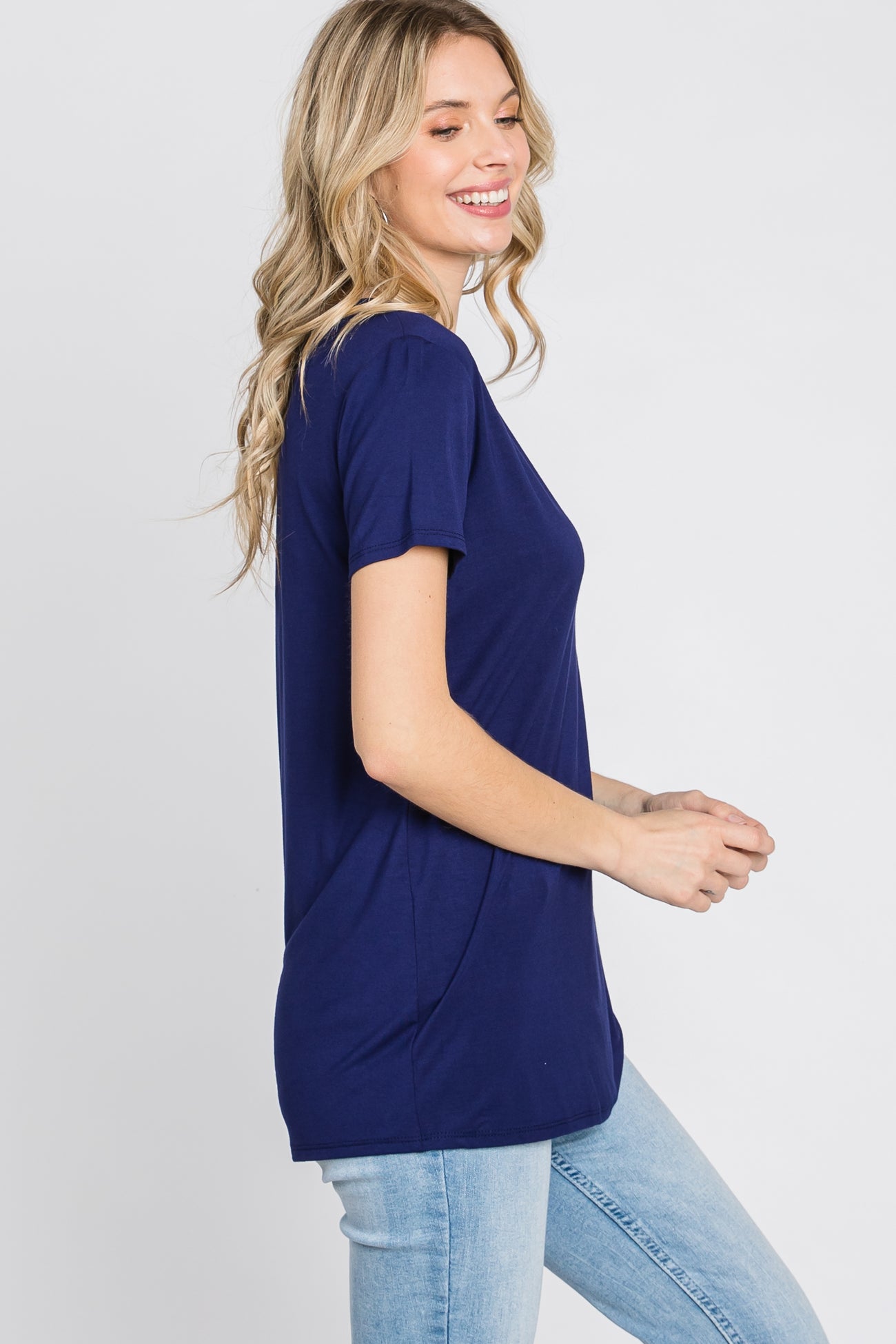 woman wearing a navy blue short sleeve t-shirt paired with light blue jeans, smiling and standing sideways
