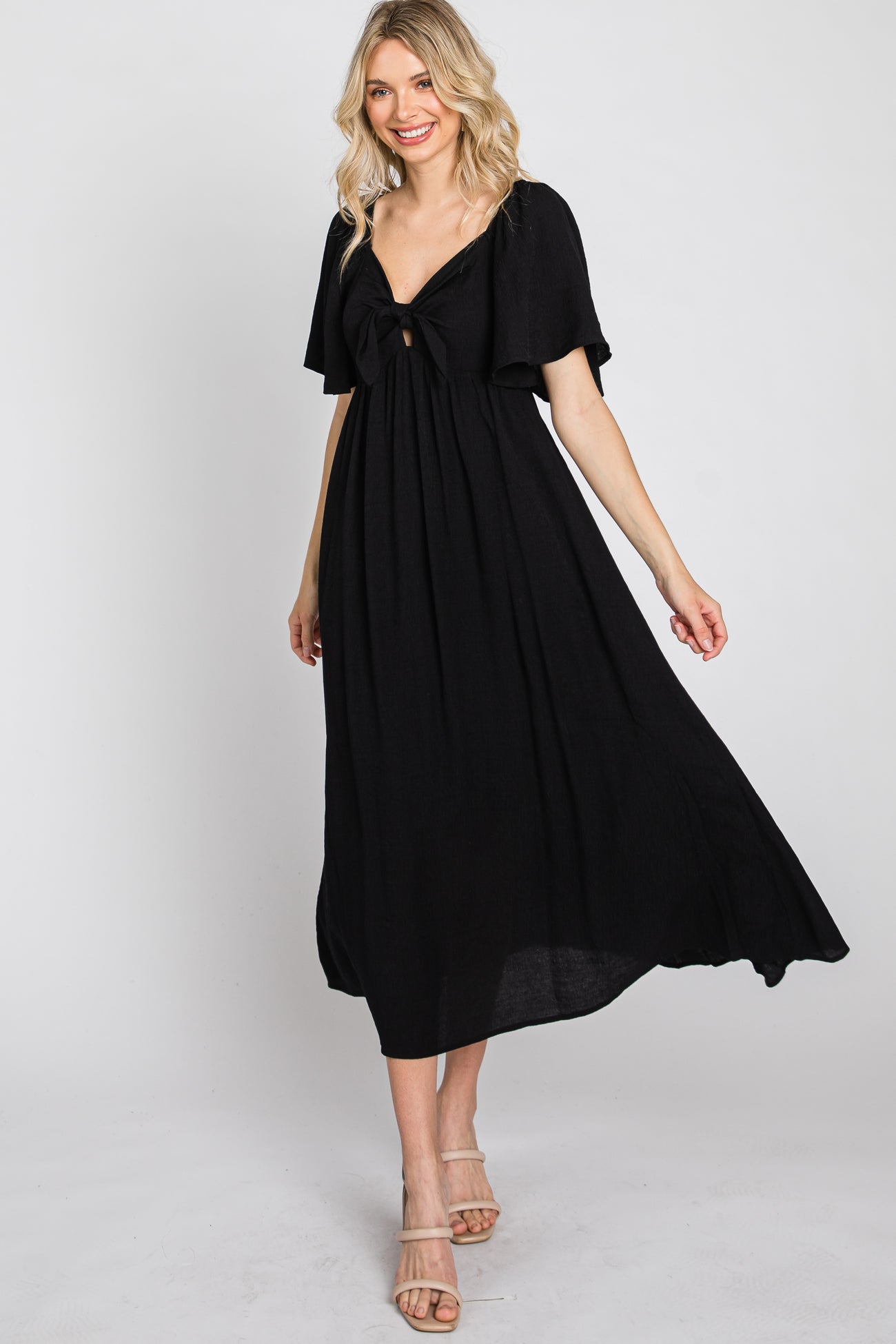 woman wearing a black maxi dress with a flutter sleeve and open tie front detail, standing confidently