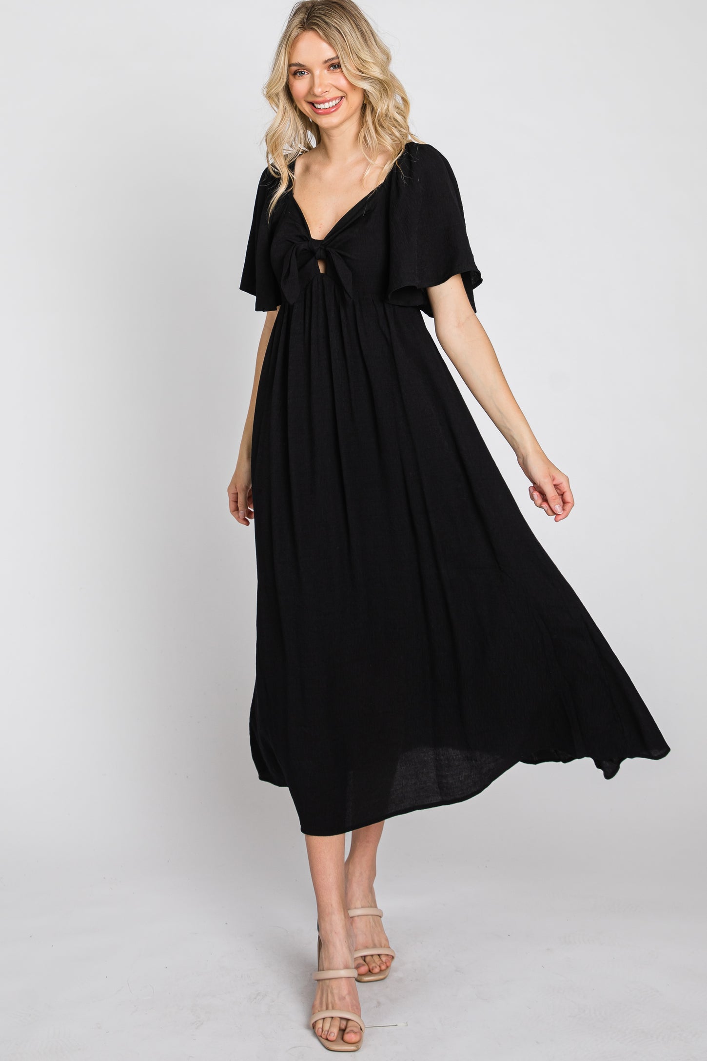 woman wearing a black maxi dress with a flutter sleeve and open tie front detail, standing confidently