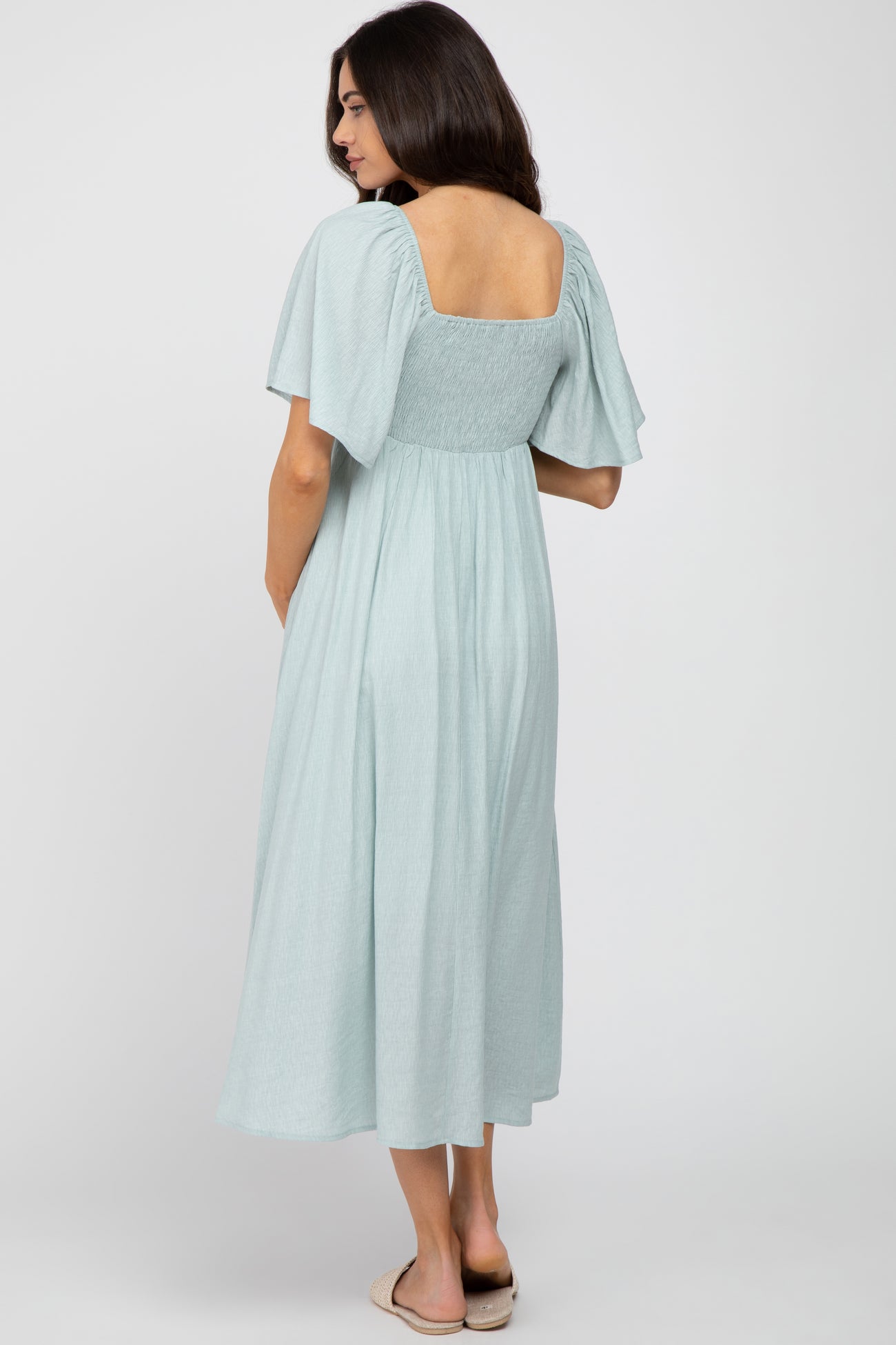 woman wearing a light green maternity dress with short puff sleeves and a square neckline, showcasing a flowing skirt