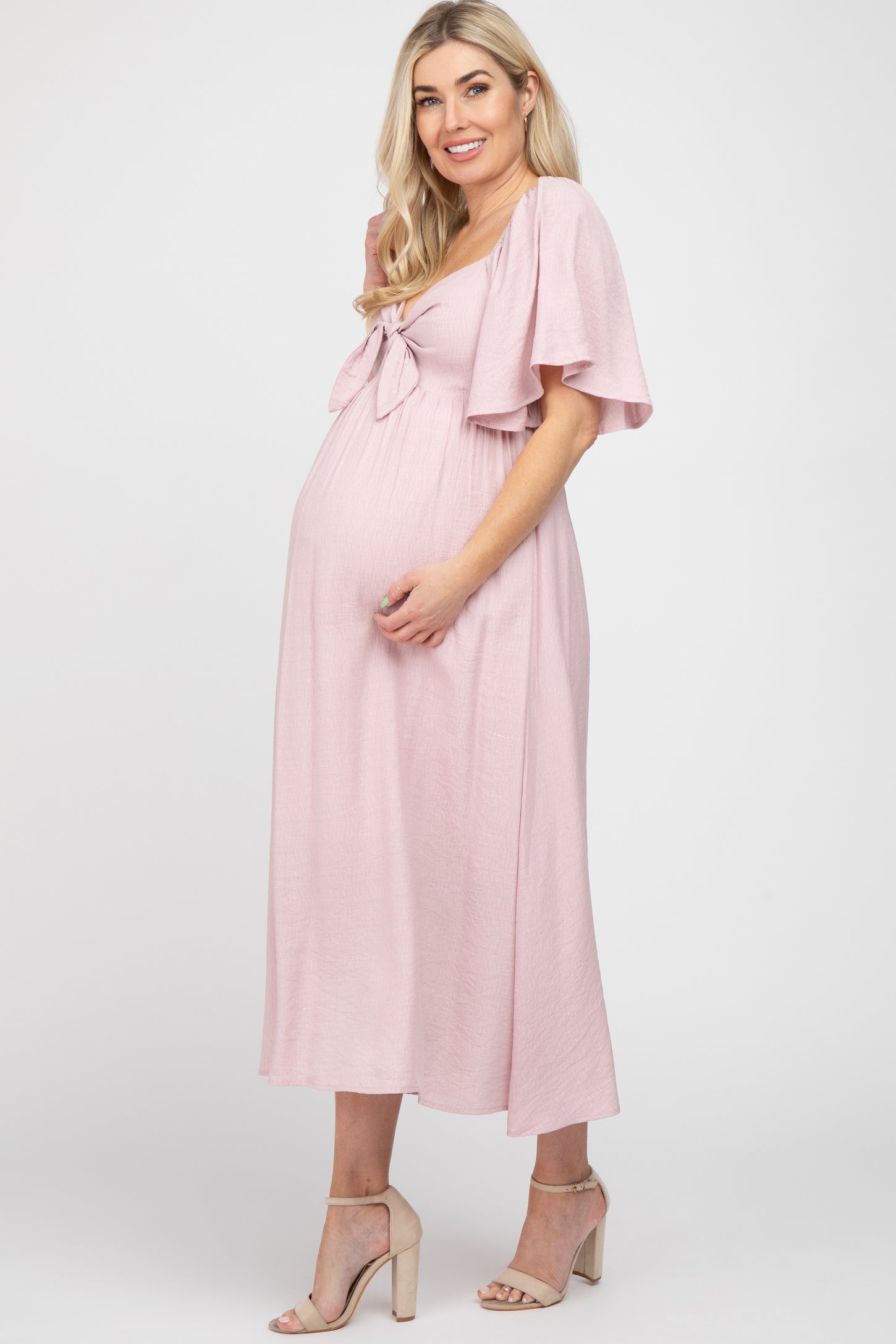 woman wearing a pink maternity dress with tie front detail and flutter sleeves, showcasing her baby bump