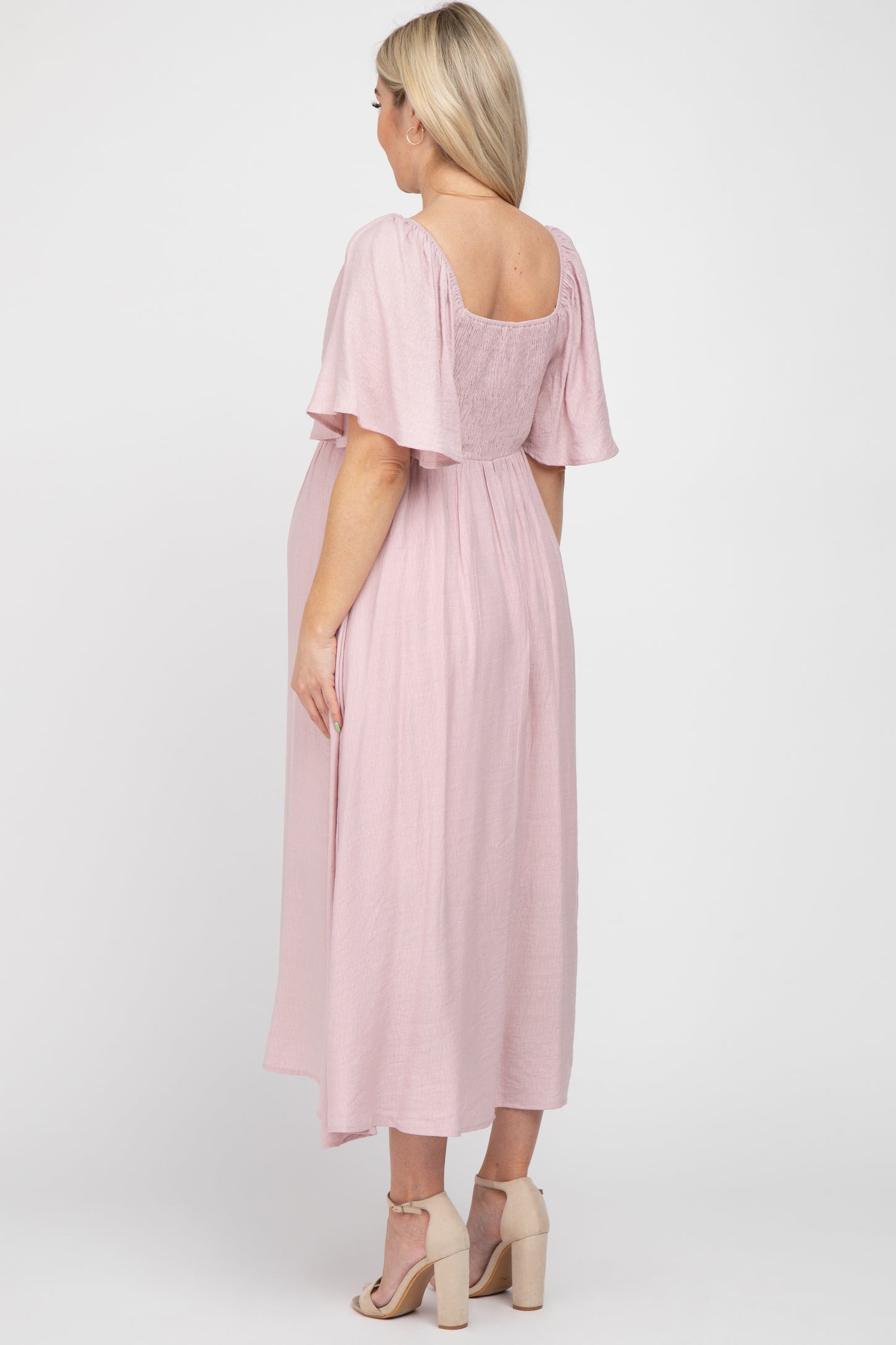 woman wearing a light pink maternity maxi dress with flutter sleeves and a visible baby bump from the back