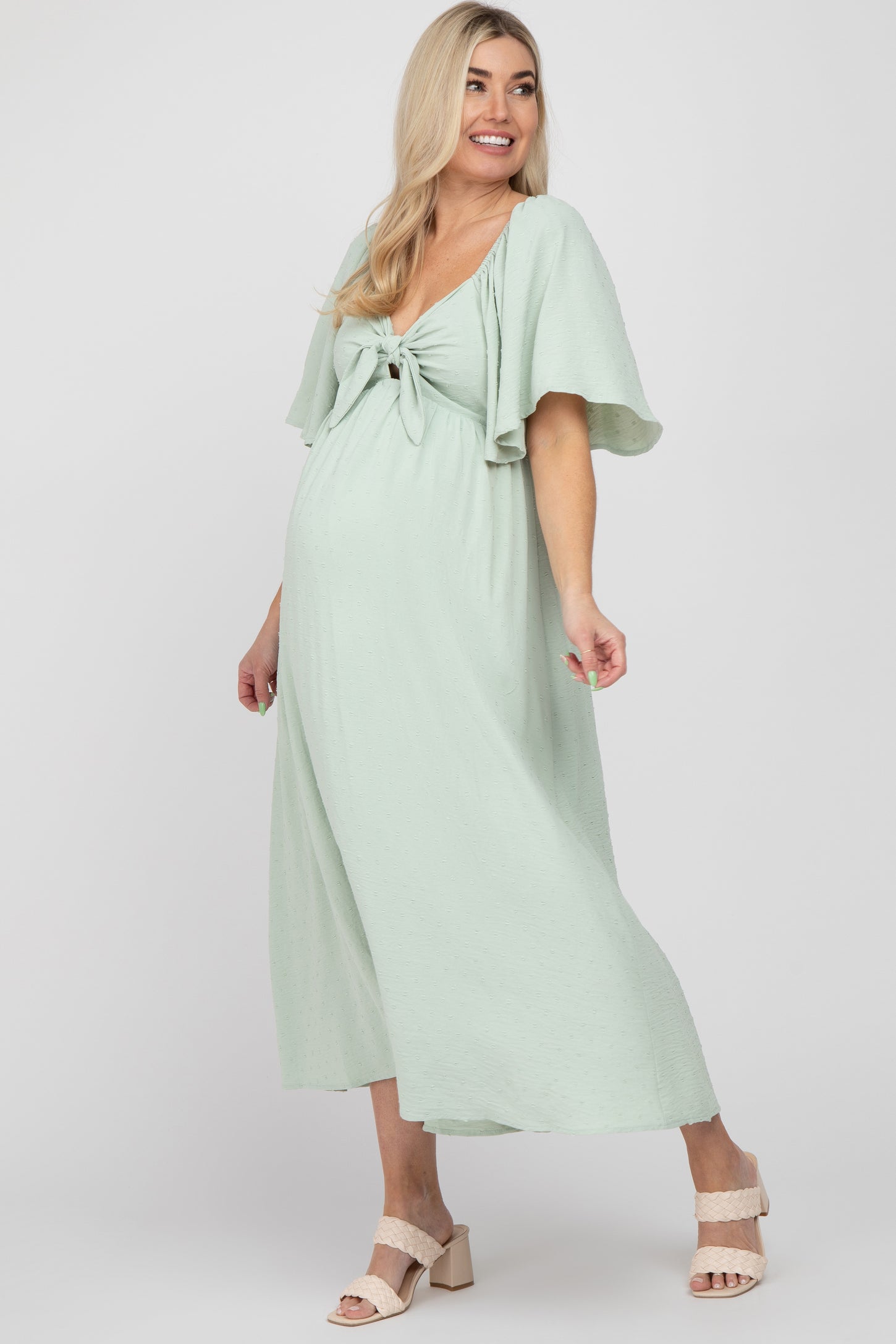 woman wearing a light green maternity dress with a tie front and flutter sleeves, showing her baby bump