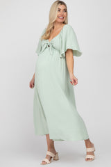woman wearing a light green maternity dress with a tie front and flutter sleeves, showing her baby bump