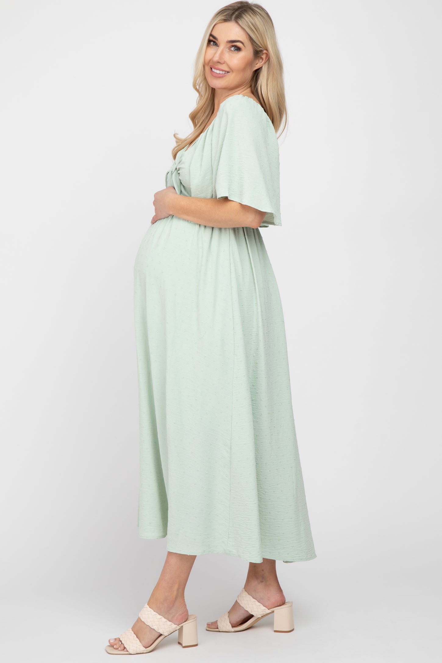 woman wearing a light green maternity dress with short sleeves and a v-neck, showing her baby bump