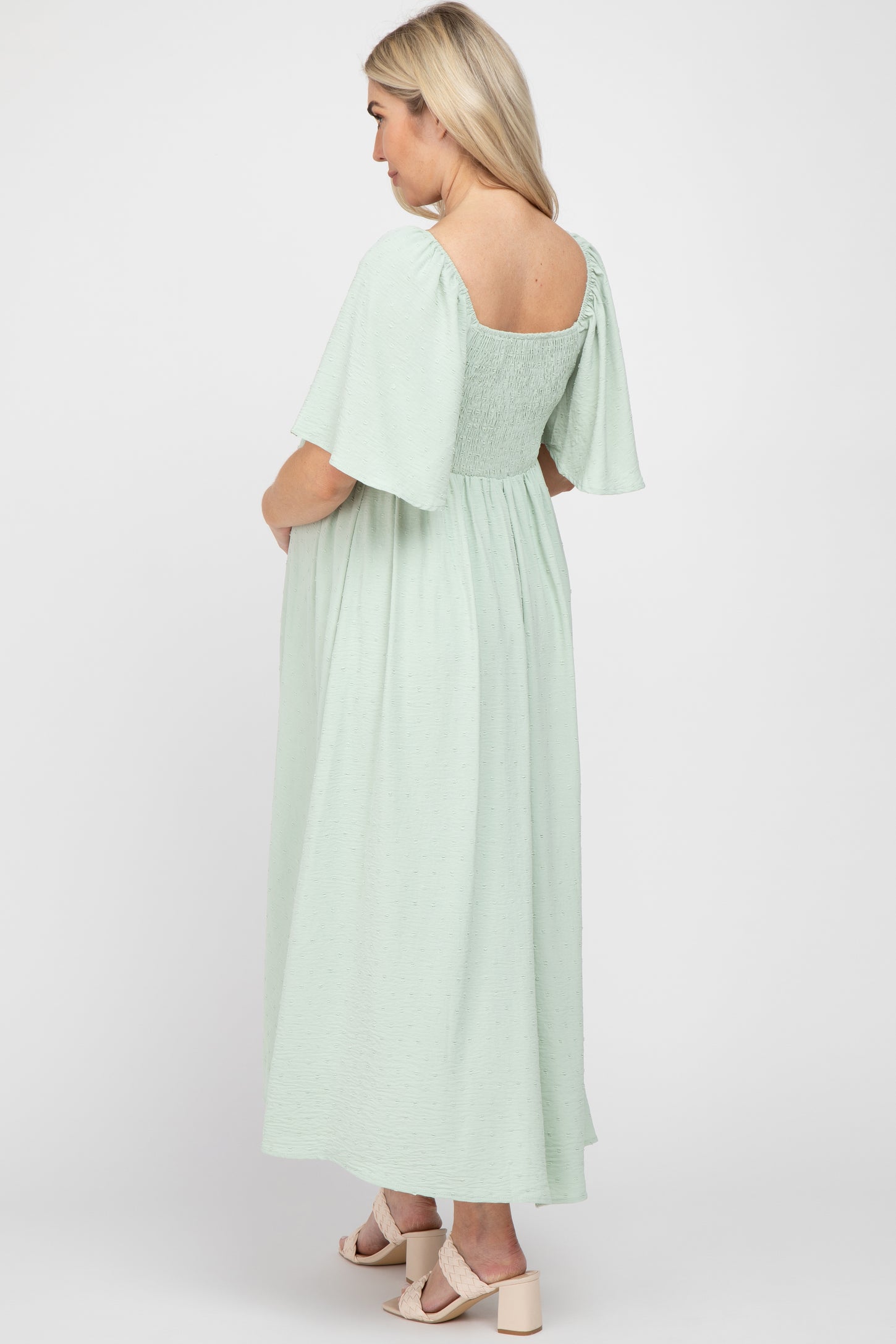 woman wearing a mint green maternity maxi dress with short flutter sleeves and a fitted bodice, showcasing her baby bump