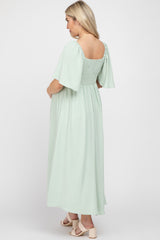 woman wearing a mint green maternity maxi dress with short flutter sleeves and a fitted bodice, showcasing her baby bump
