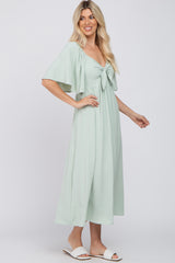 woman wearing a mint green flutter sleeve maxi dress with a front knot detail and styled with white slip-on sandals